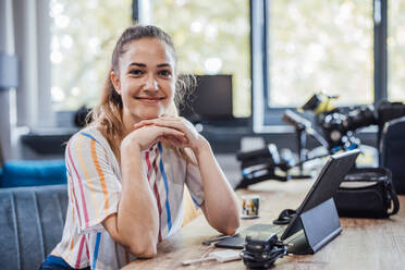 Smiling businesswoman with hand on chin sitting at desk - JOSEF17528