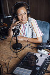 Junge Podcast-Künstlerin mit Kopfhörern, die im Studio in ein Mikrofon spricht - JOSEF17532