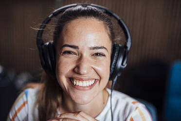 Happy young podcaster wearing headphones in studio - JOSEF17537