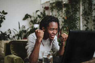 Freelancer cheering on video call through laptop at home office - MDOF00744