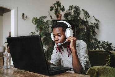 Freiberufler mit Headset sitzt mit Laptop im Home Office - MDOF00747