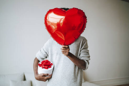 Man covering face with heart shape balloon at home - MDOF00777