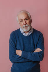 Senior man with arms crossed standing against pink background - MDOF00778