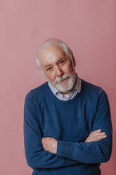 Elderly man with arms crossed against pink background - MDOF00780