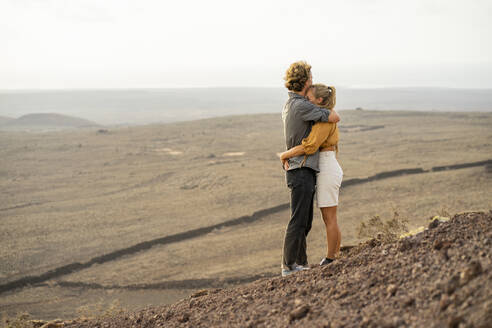 Romantisches junges Paar, das sich auf einem Berg stehend umarmt - FBAF02104