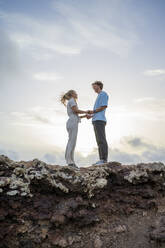 Young couple standing on cliff holding hands - FBAF02113