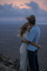 Romantische Frau, die ihren Freund bei Sonnenuntergang umarmt - FBAF02119