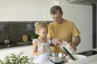 Älterer Mann misst mit seiner Enkelin in der Küche Mehl ab - SVKF01313