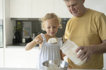Lächelndes Mädchen hält Mehl in einem Löffel bei seinem Großvater zu Hause - SVKF01314