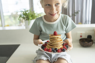 Mädchen hält einen Stapel Pfannkuchen mit Beeren in der Küche - SVKF01328