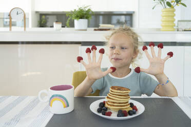 Mädchen mit Himbeeren an den Fingern sitzt am Esstisch in der Küche - SVKF01330