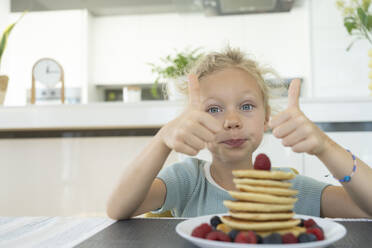 Mädchen macht Daumen hoch Geste durch Teller mit frischen Pfannkuchen zu Hause - SVKF01333