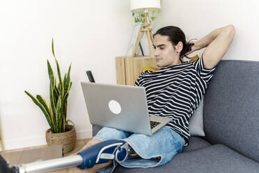 Young man with amputated leg using smart phone on sofa at home - JCZF01210