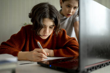 Junge macht Hausaufgaben mit Bruder im Hintergrund zu Hause - ANAF01062