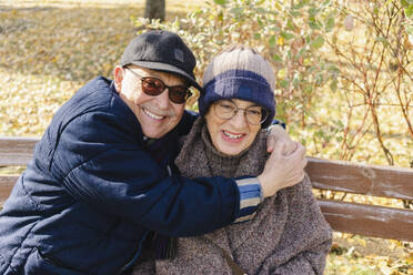 Happy senior man embracing woman sitting on bench - SEAF01756