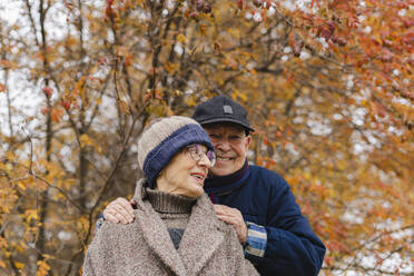 Happy senior man with hands on shoulders of woman under tree - SEAF01775