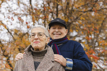 Smiling elderly couple under tree at autumn park - SEAF01776