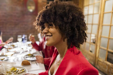 Glückliche Frau mit Afrofrisur beim Abendessen im Restaurant - JCCMF09580