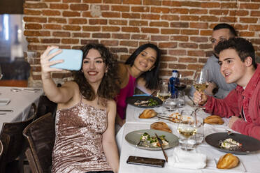 Glückliche Frau nimmt Selfie mit Freunden im Restaurant - JCCMF09610