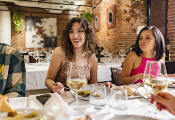 Happy women enjoying dinner with friends at restaurant - JCCMF09621