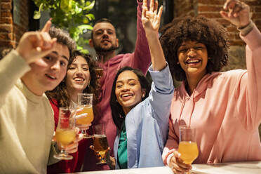 Happy multiracial friends with hands raised enjoying at restaurant - JCCMF09657