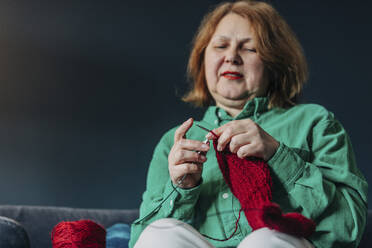 Elderly woman knitting red sweater with needle at home - VSNF00565