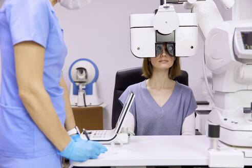 Arzt mit Patient bei der Überprüfung der Sehkraft durch den Phoropter in der Klinik - SANF00073