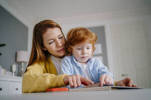 Rothaarige Frau liest mit ihrem Sohn zu Hause ein Buch - MDOF00793