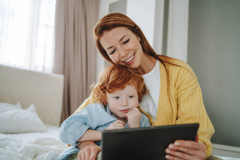 Glückliche Frau, die mit ihrem Sohn zu Hause auf einen Tablet-PC schaut - MDOF00803