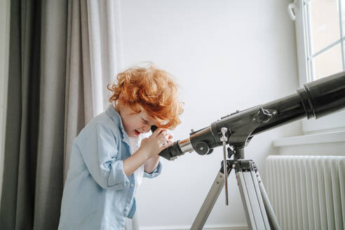 Curious boy looking through telescope at home - MDOF00810