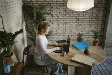Geschäftsfrau bei der Arbeit mit einem Laptop am Schreibtisch am Arbeitsplatz - RCPF01724