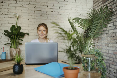Smiling businesswoman behind laptop at workplace - RCPF01726