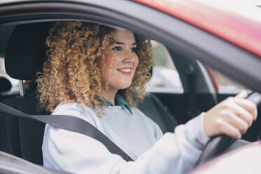 Smiling woman with curly hair driving car - AMWF01175