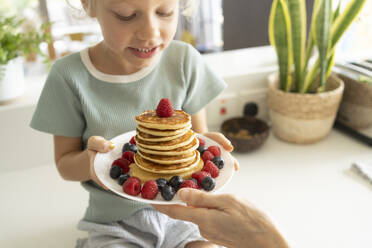 Girl holding stack of fresh pancakes on plate at home - SVKF01336
