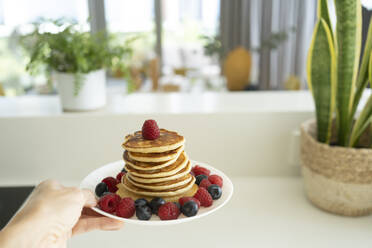 Hand holding stack of fresh pancakes on plate at home - SVKF01338