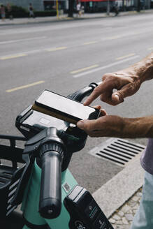 Close-up of hand unlocking electric push scooter using smart phone - MASF35429