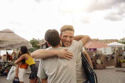 Glücklicher junger Mann umarmt männlichen Freund mit Frauen umarmen im Hintergrund - MASF35431