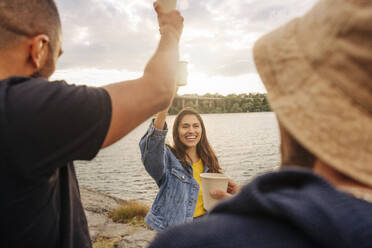 Happy woman wearing denim jacket toasting drinks with friends during picnic - MASF35438