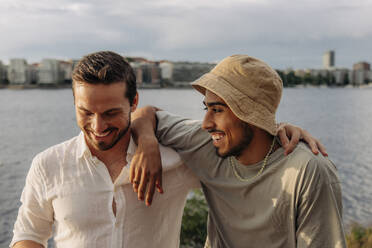 Glückliche männliche Freunde mit Arm um einander reden gegen das Meer - MASF35441