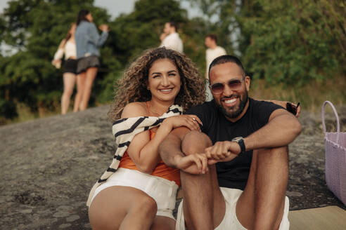 Porträt einer glücklichen Frau auf einem Felsen sitzend mit einem Mann mit Sonnenbrille beim Picknick - MASF35457
