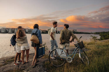 Multiracial male and female friends standing and talking on rock by sea during sunset - MASF35465