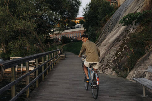 Glücklicher junger Mann, der beim Radfahren auf dem Pier über die Schulter schaut - MASF35468