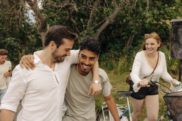 Happy woman with bicycle looking at male friends walking together - MASF35471