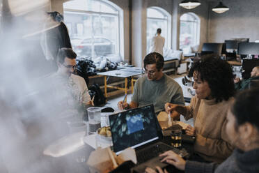 Geschäftsmann bei der Arbeit inmitten von männlichen und weiblichen Kollegen am Schreibtisch in einem kreativen Büro - MASF35477