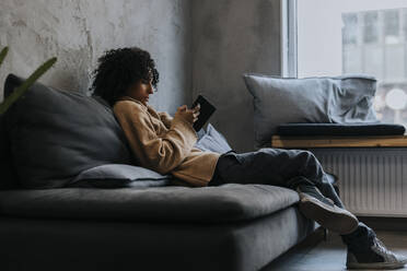 Geschäftsfrau schreibt Textnachrichten über ihr Mobiltelefon, während sie auf dem Sofa eines Start-up-Unternehmens sitzt - MASF35493