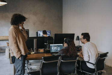 Businesswoman discussing with male and female programmers working on laptop at desk - MASF35511