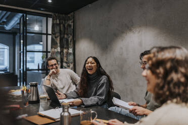 Cheerful multiracial colleagues discussing at conference table in board room - MASF35544