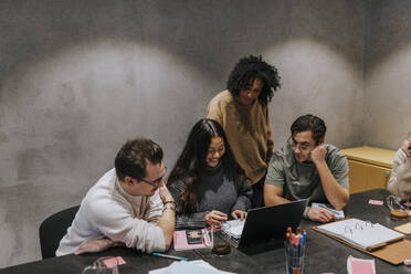 Multiracial male and female colleagues discussing over laptop at conference table in office - MASF35547