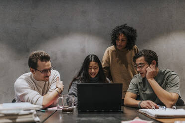 Männliche und weibliche Geschäftskollegen diskutieren über Laptop am Konferenztisch in einem Startup-Unternehmen - MASF35548