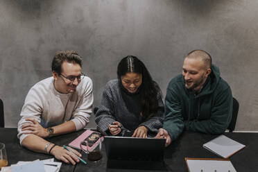 Smiling businesswoman discussing strategy over laptop with male colleagues at workplace - MASF35549